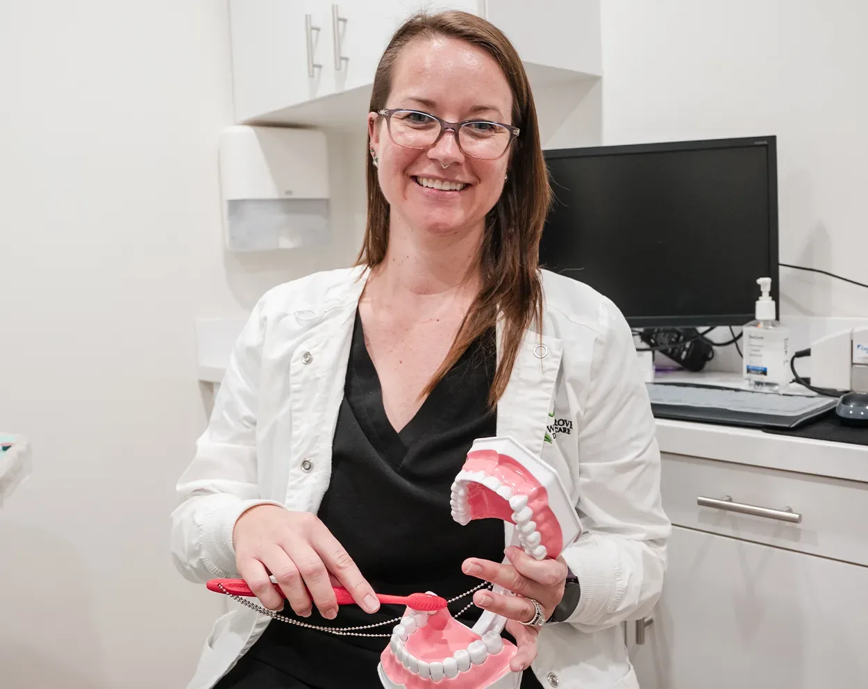 A smiling hygienist holding a toothbrush and a model of teeth