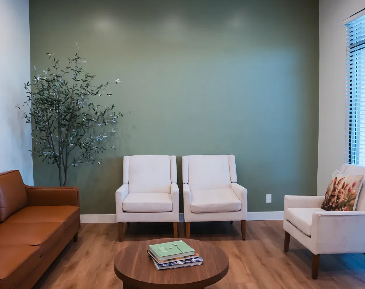A comfortable waiting area with a leather sofa, armchairs, and a plant against a green wall