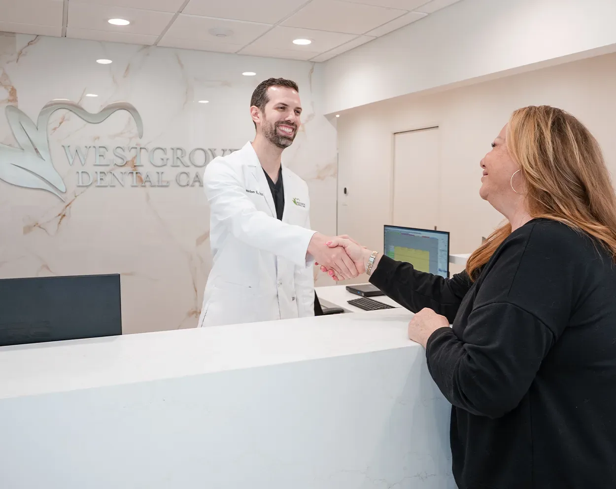 A Westgrove Dental Care dentist shaking hands with a patient at the front desk