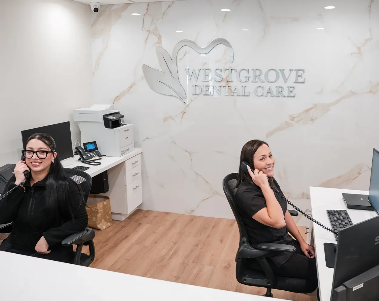 Two front office team members seated at their desks in front of the marble logo wall
